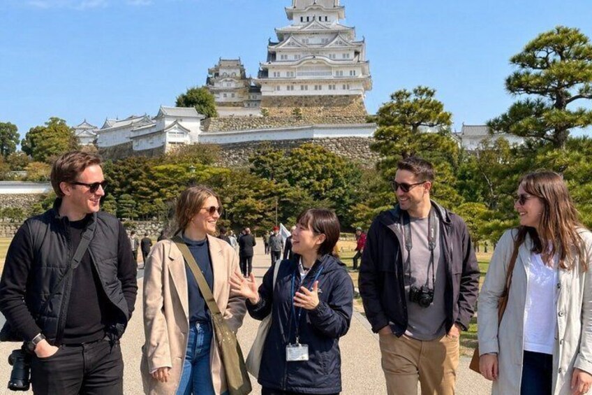 A group of people standing in front of a castle-like structure with multiple tiers and a prominent tower. 3