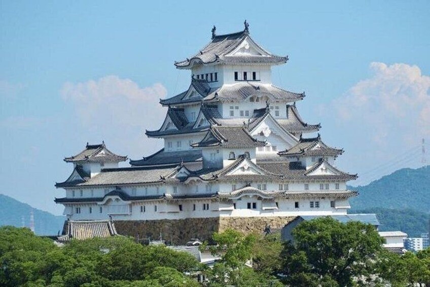 A multi-tiered castle with traditional architecture, surrounded by greenery and mountains in the background. 2