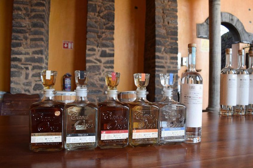 A row of liquor bottles on a wooden table with stone walls and a brick archway in the background. 5