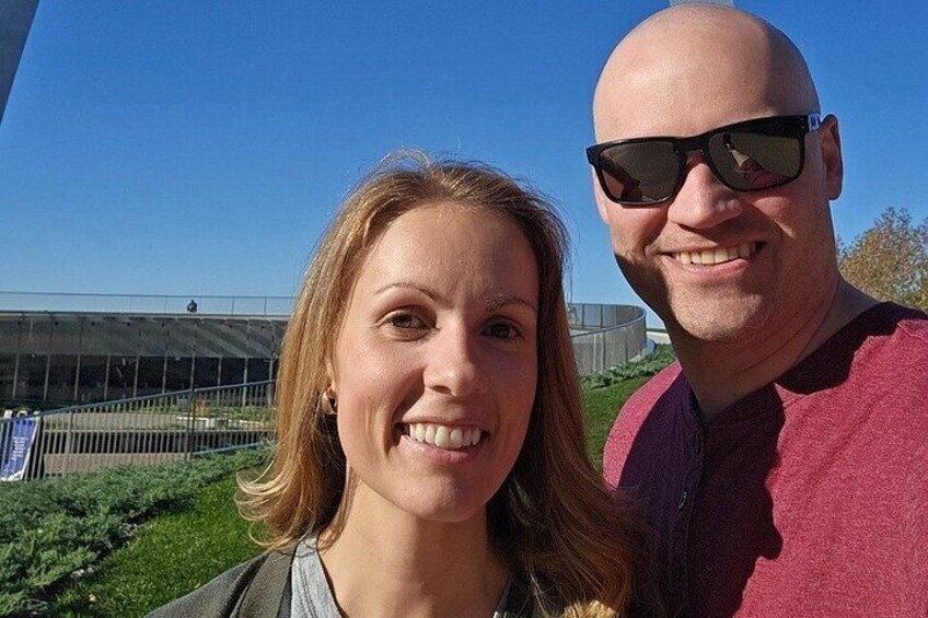 Deux personnes se tiennent à l’extérieur, avec un bâtiment et de la végétation en arrière-plan. 4