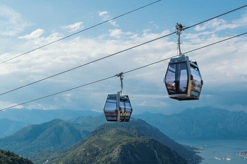 Two cable cars suspended over a mountainous landscape with a body of water below. 1