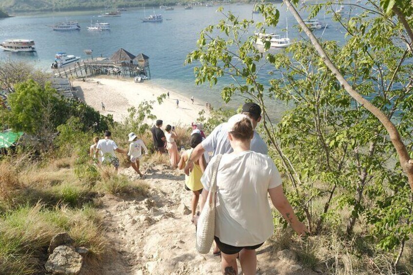 Eine Gruppe von Wanderern geht einen sandigen Pfad entlang Richtung Strand, wo Boote im Wasser liegen. 5