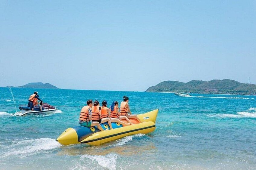 A group of people on a yellow inflatable raft in the ocean, with a jet ski in the background. 4