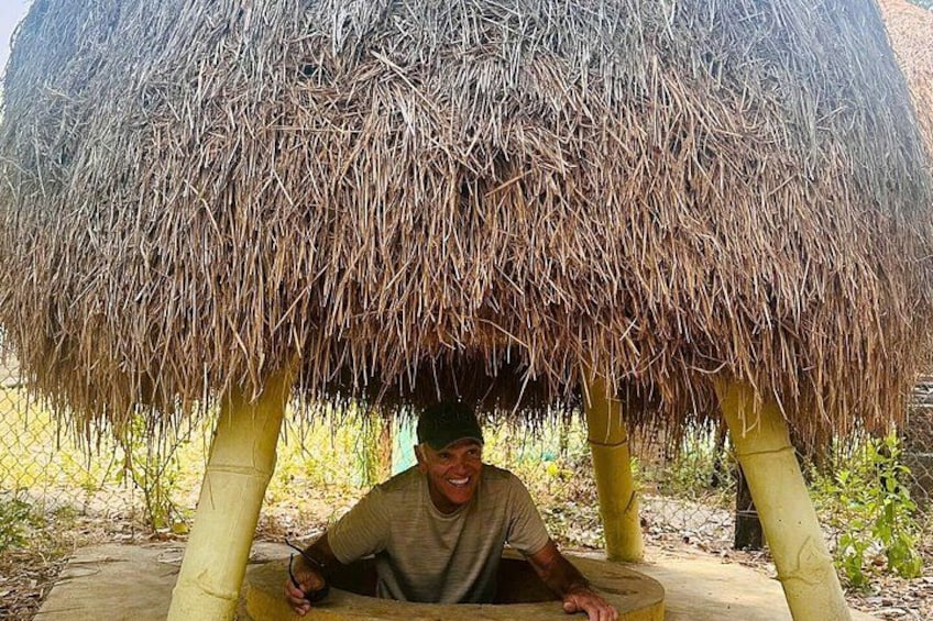 A person sitting under a thatched structure with a natural landscape in the background. 2