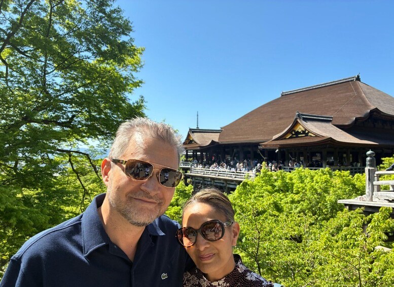 A man and a woman standing in front of a traditional Japanese building with a curved roof and a wooden structure in the background. 3