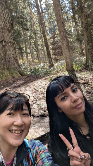 Two people in a forest with tall trees and a wooden structure in the background. 5