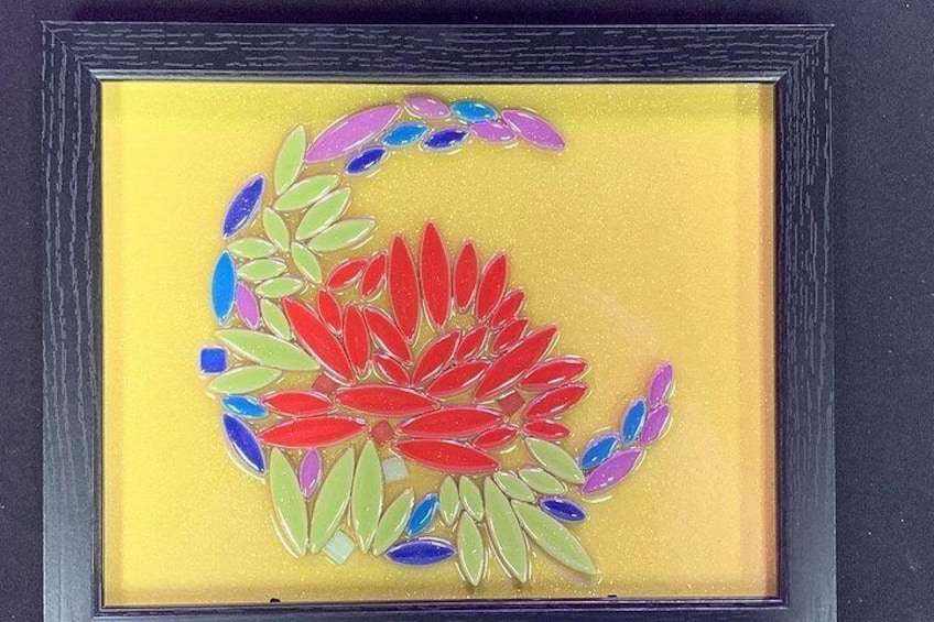 A framed artwork with a yellow background and a red flower with green and blue leaves. 3