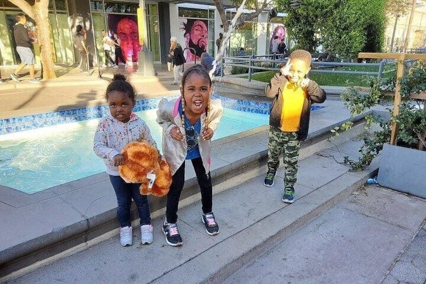 Three children standing by a pool with a sculpture in the background. 2