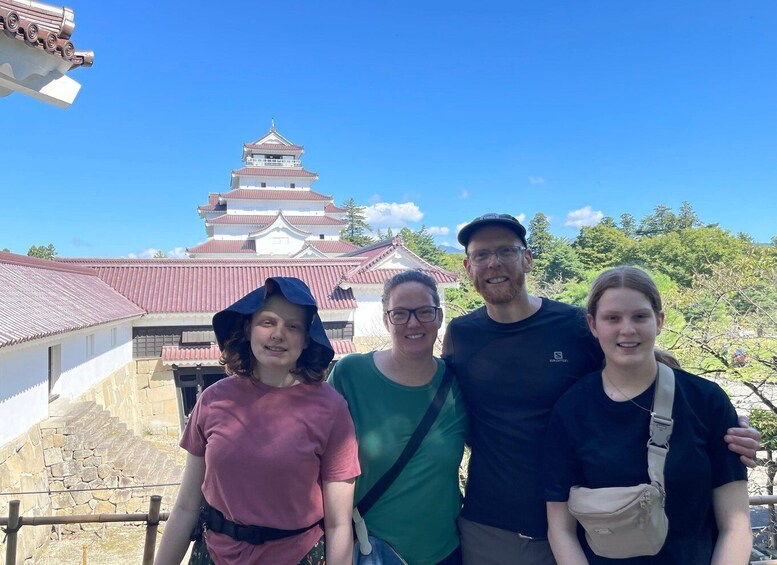 A group of people standing in front of a traditional Japanese castle with a red roof and multiple tiers. 5