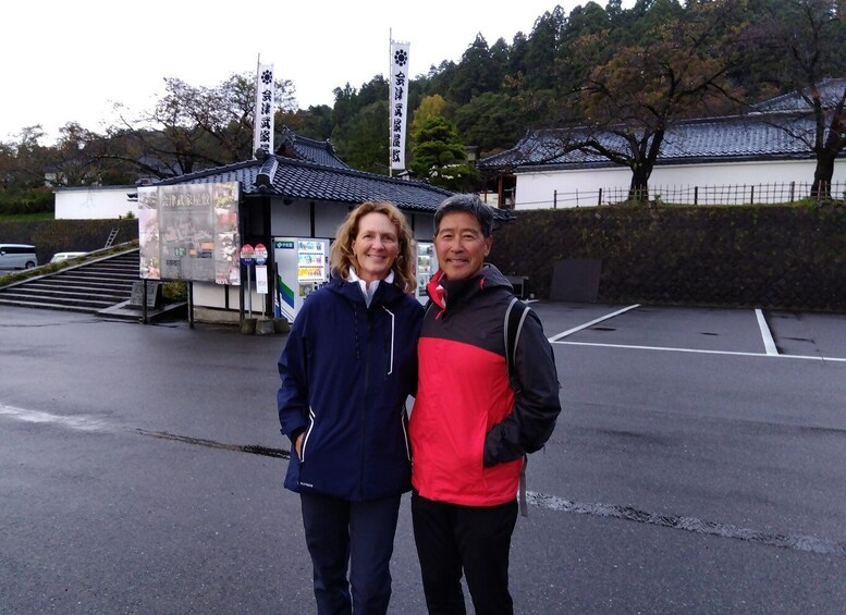 Two people standing in front of a traditional Japanese building with a tiled roof and a white wall. 5
