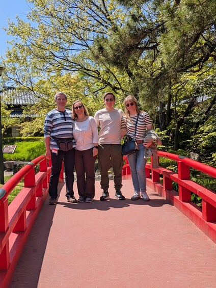 Four people standing on a red bridge with greenery in the background. 4