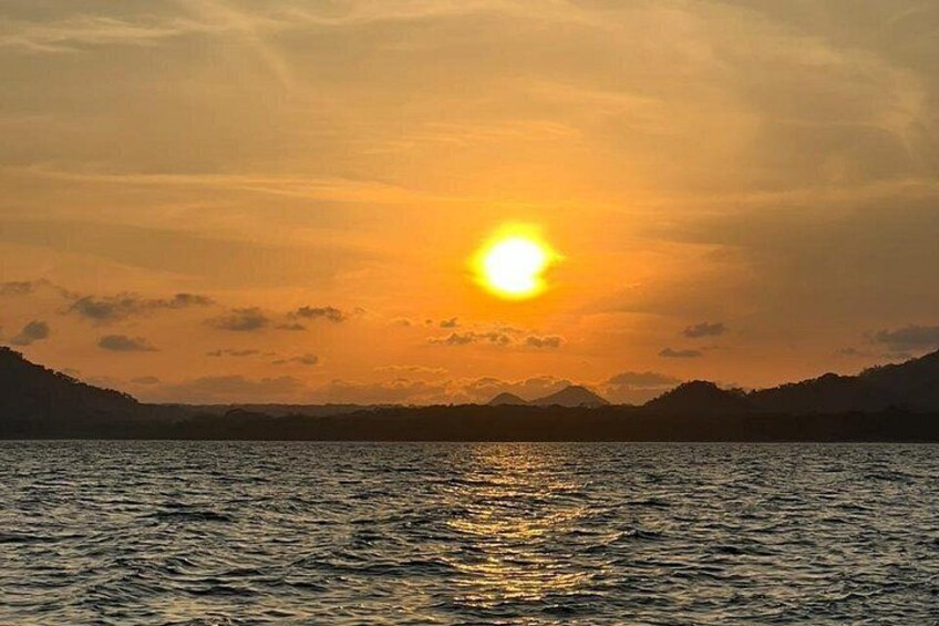 A sunset over a body of water with mountains in the background. 1