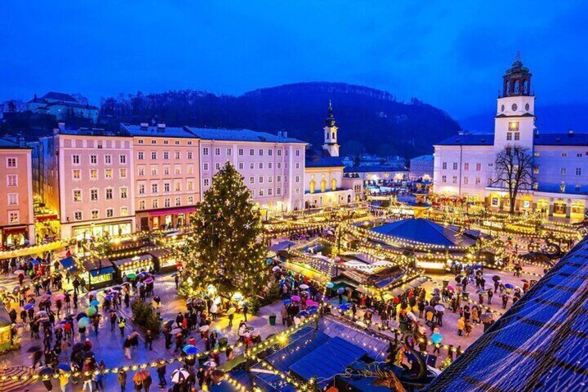 A festive market square with illuminated buildings and a large Christmas tree. 5