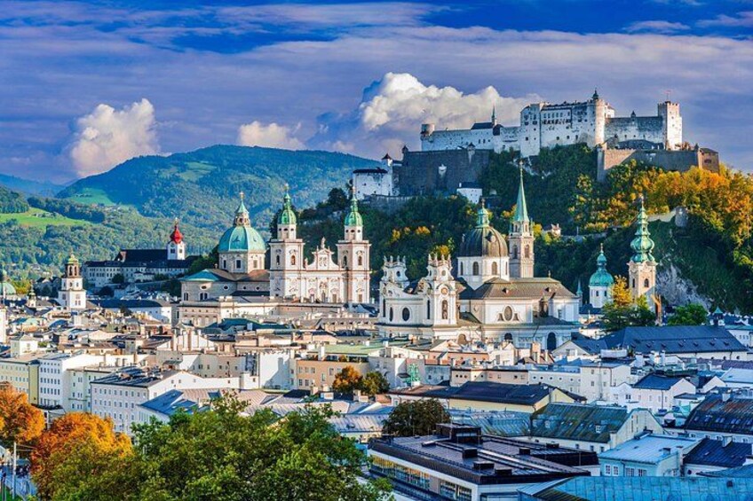 A cityscape with a prominent cathedral, a castle on a hill, and surrounding greenery. 1