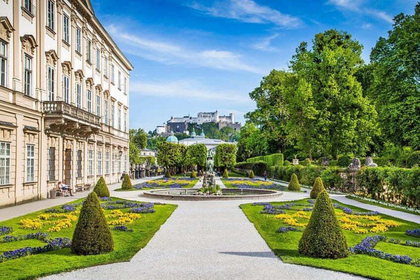 A formal garden with manicured lawns, geometric hedges, and a central pathway leading to a building. 3