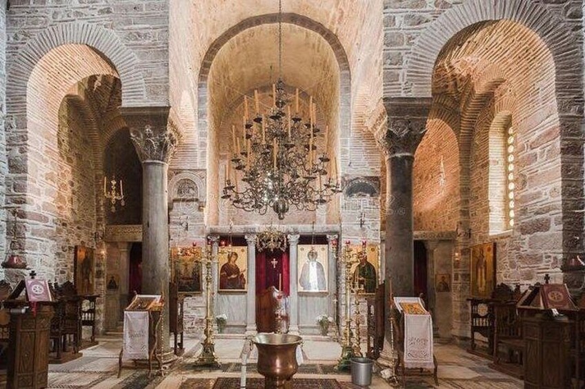 An interior of a historic building with stone arches, a central chandelier, and religious icons. 4