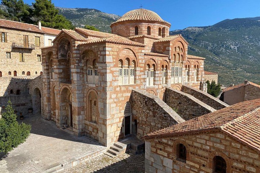 A historic stone building with a dome and arches, surrounded by other buildings and mountains in the background. 2