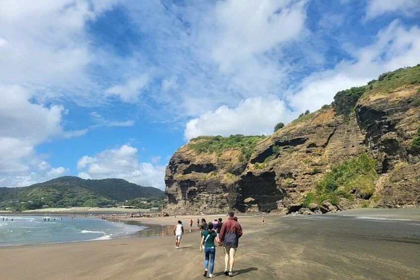 A beach with people walking, a rocky cliff, and a clear sky. 2