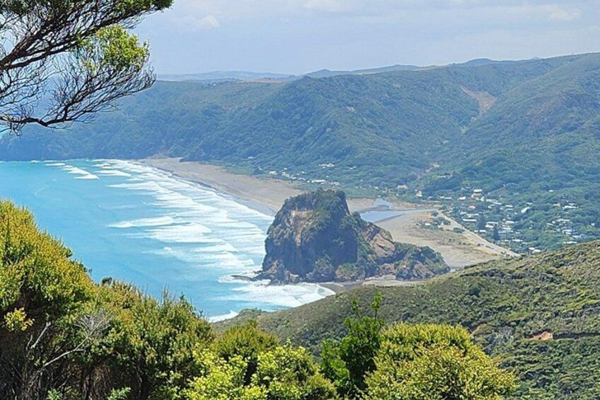 A coastal landscape with a prominent rock formation, a beach, and a town in the distance. 2