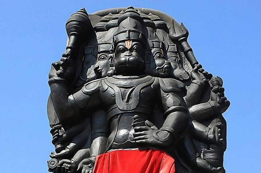A large, detailed statue of a deity with multiple arms, wearing red garments, set against a clear blue sky. 5