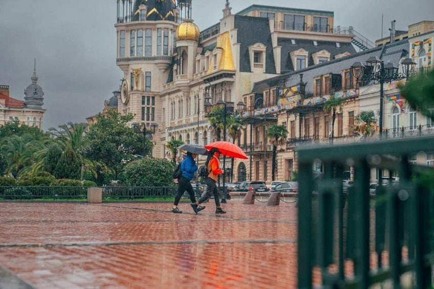 A historic building with a clock tower and a dome, pedestrians walking on a cobblestone path, and a red umbrella held by one person. 5