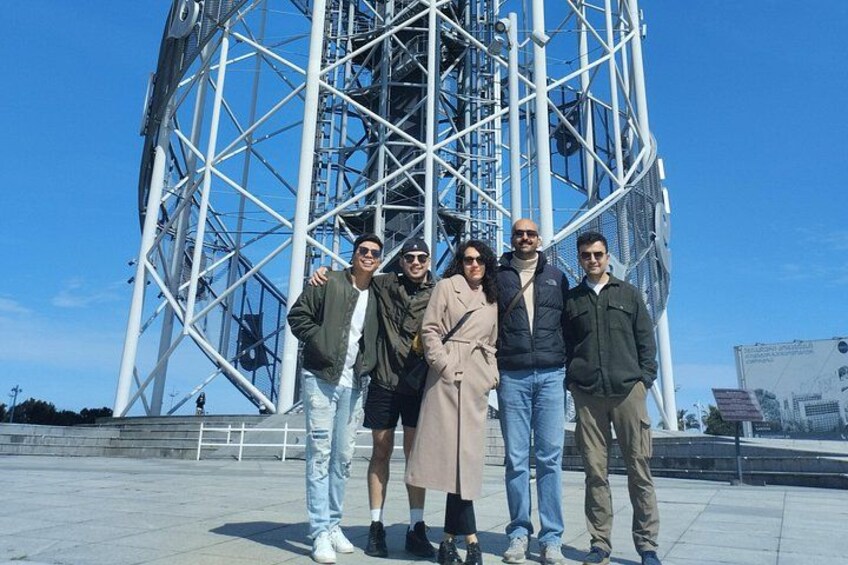 A group of people standing in front of a large metal structure with a lattice framework. 3