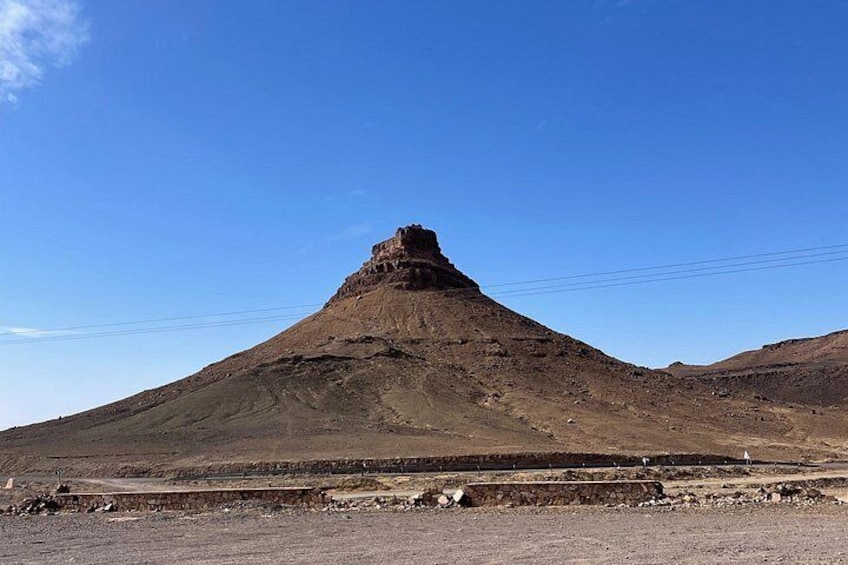A large, isolated mountain with a flat top, surrounded by barren land and a clear blue sky. 3