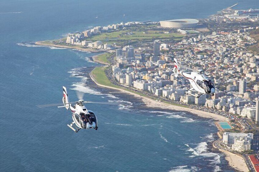 Zwei Hubschrauber fliegen über einer Küstenstadt mit Gebäuden und einem Strand. 2