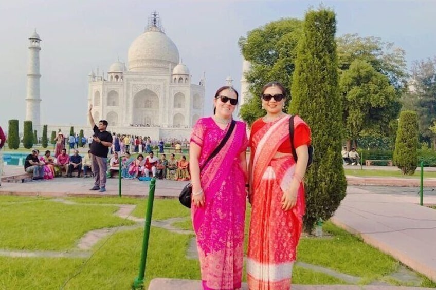 Twee vrouwen in traditionele kleding staan voor de Taj Mahal. 2