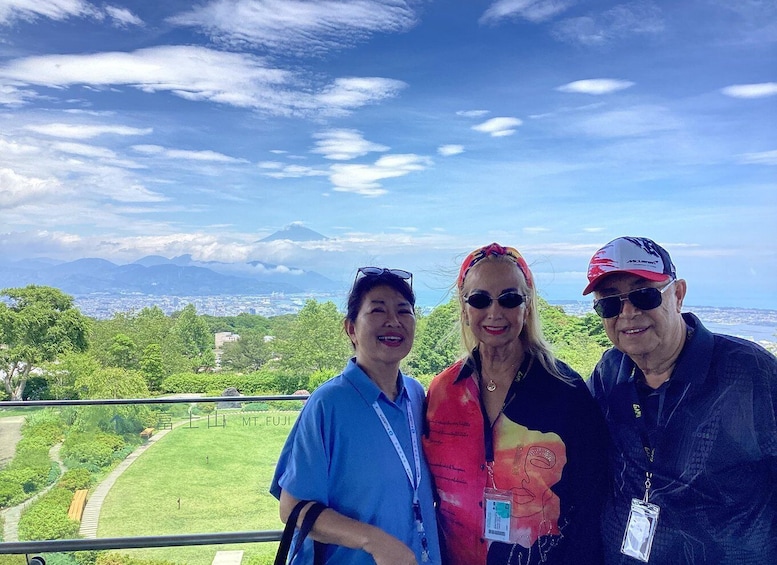 Three people standing on a balcony with a scenic view of a city and mountains in the background. 4