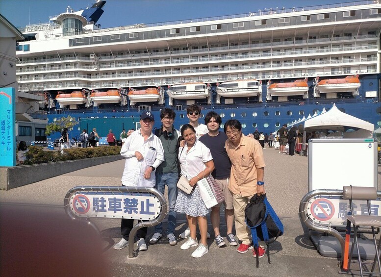 A group of people posing in front of a cruise ship with lifeboats visible. 5