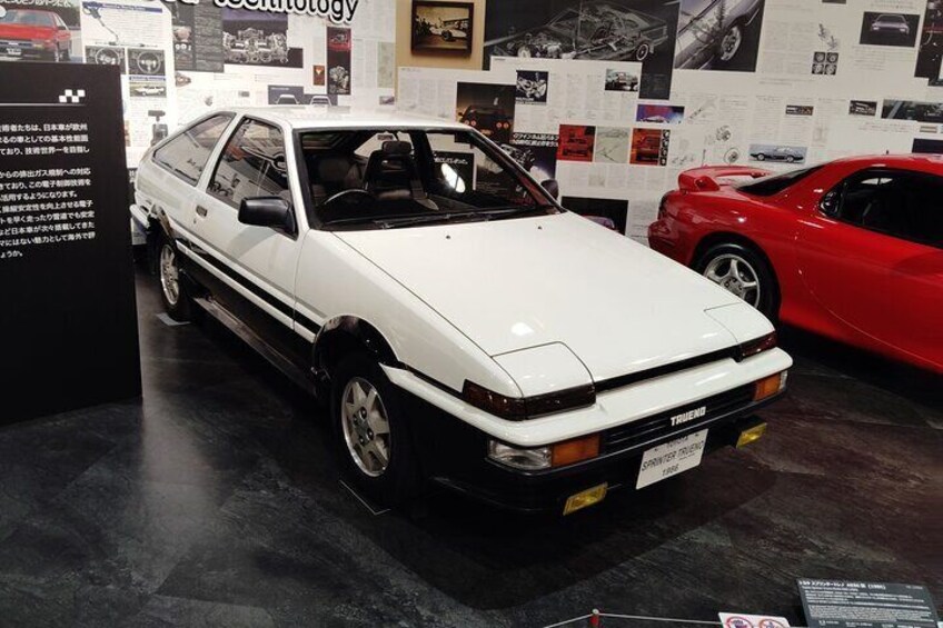 A white car with a black stripe, red and white stripes on the wheels, and a license plate. 4