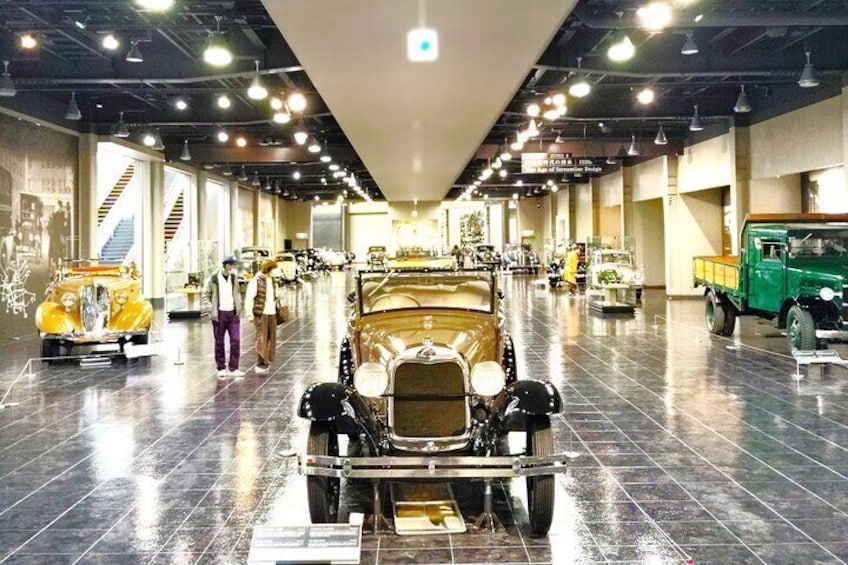 A museum with vintage cars on display, a staircase, and a green truck. 1