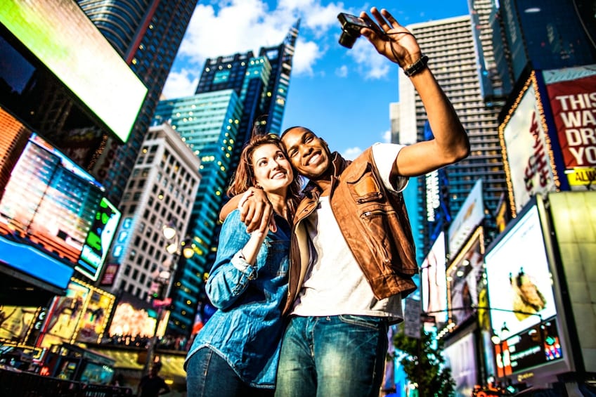 A couple taking a selfie in a bustling cityscape with tall buildings and bright billboards. 2