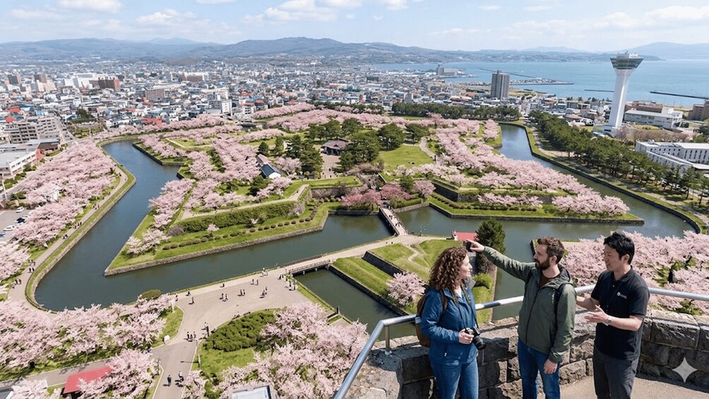 A cityscape with a river, cherry blossoms, and a tower. 1