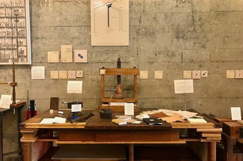A wooden desk with papers, a typewriter, and a mirror. There are numbered labels on the wall. 3