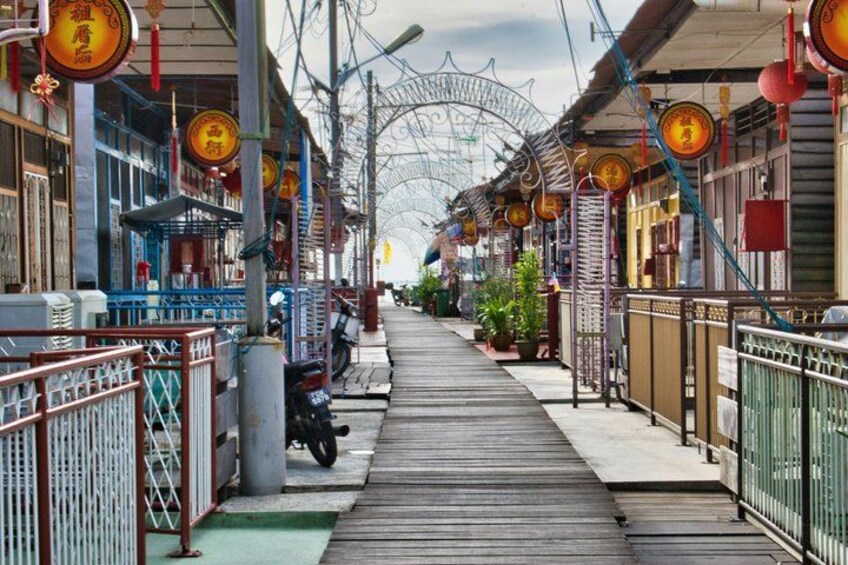 A wooden walkway flanked by traditional buildings with decorative lanterns and a metal archway in the distance. 2