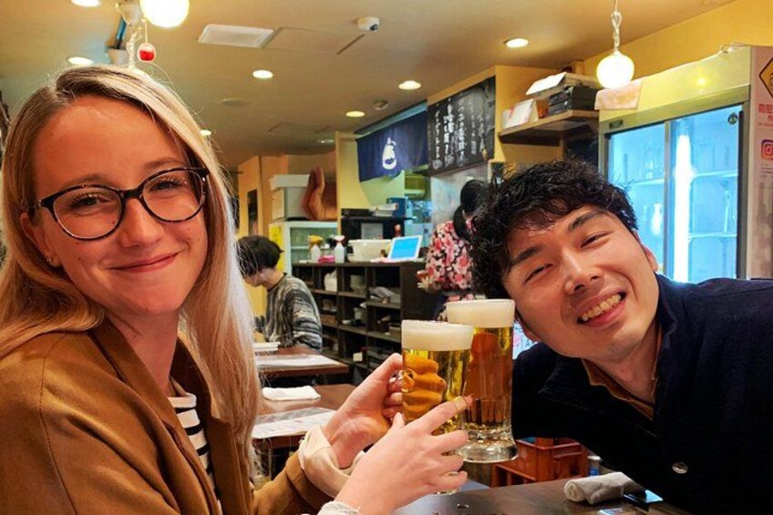 Two people toasting with beer glasses in a restaurant with visible menu boards and other patrons in the background. 4