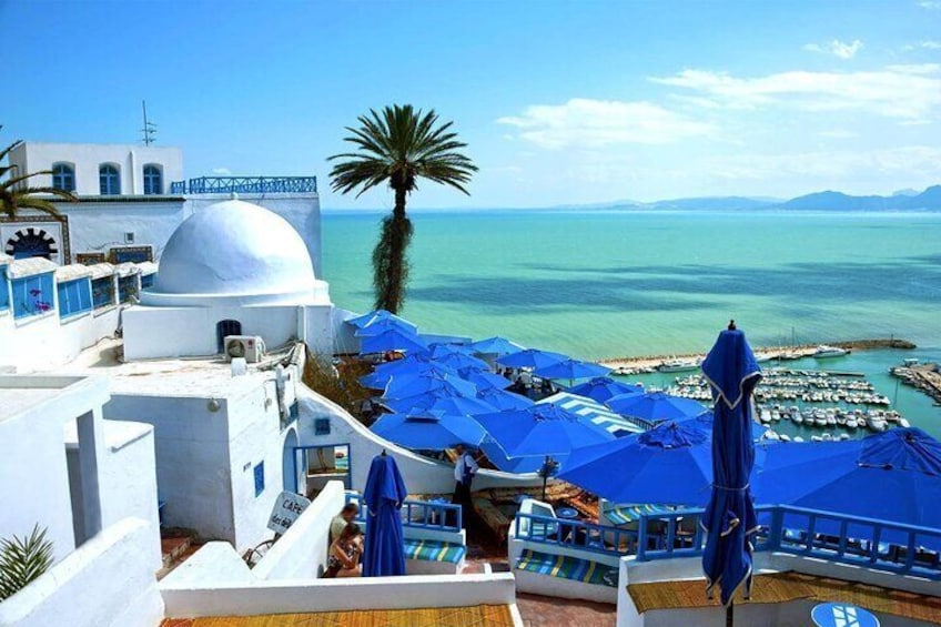 A coastal town with white buildings, blue umbrellas, and a clear view of the sea. 3