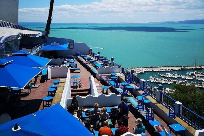 A seaside restaurant with blue umbrellas and tables overlooking the ocean and marina. 5