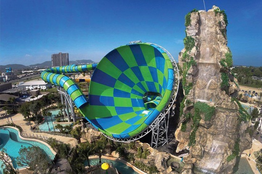 A large water slide with a checkered pattern, a pool, and a rocky cliff. 1