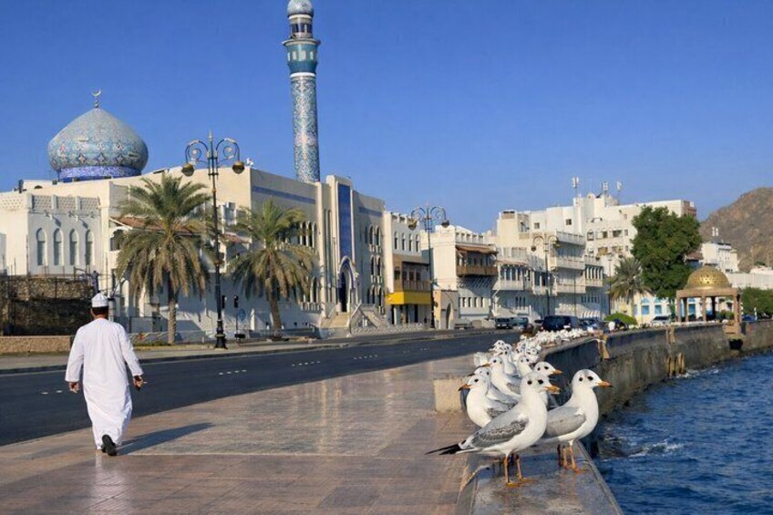 A mosque with a minaret, palm trees, and seagulls by the water. 3