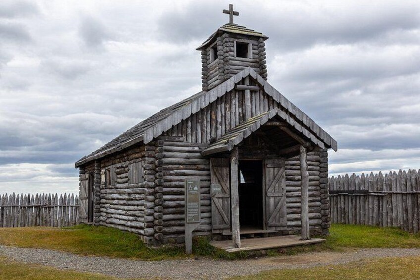 A wooden log cabin with a cross on top, a small bell tower, and a wooden fence in the background. 3