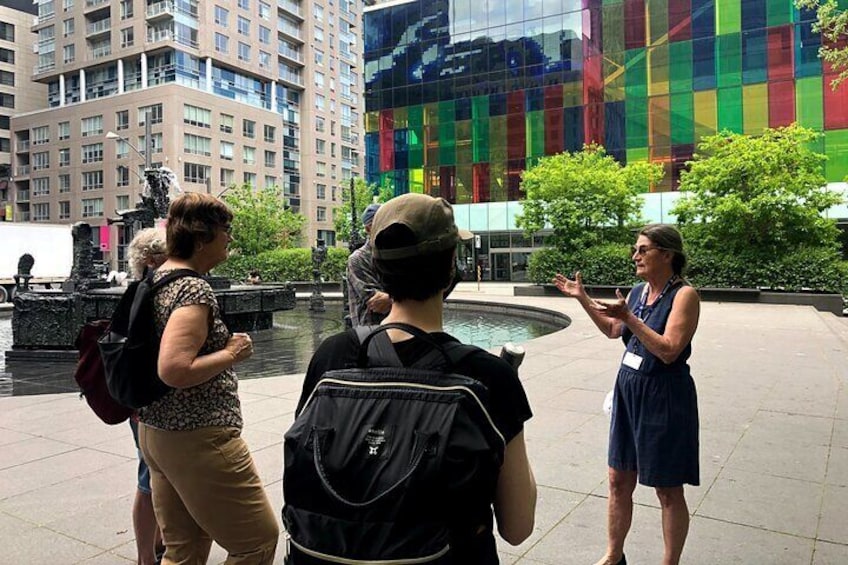 Three people standing in a plaza with a fountain and modern buildings in the background. 5