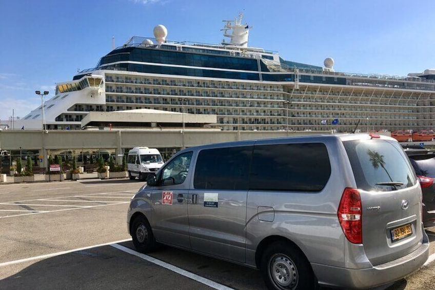 A silver minivan parked in a lot with a large cruise ship in the background. 4