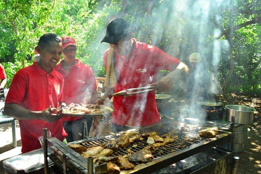 A group of people grilling food outdoors with a grill and cooking utensils. 2