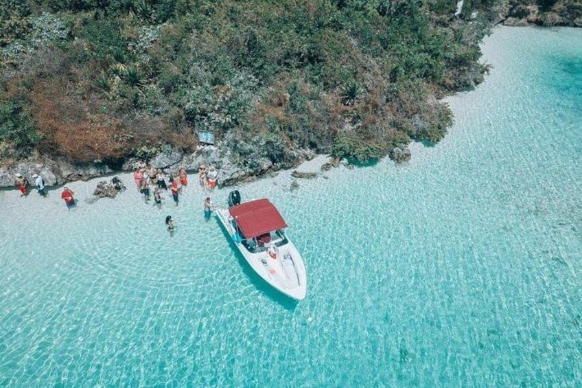 A boat with a red canopy on a clear turquoise sea, surrounded by rocky shores and dense vegetation. 1