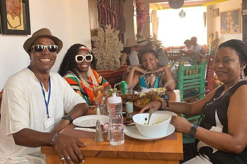 A group of people dining at a wooden table with bowls of food, glasses, and a bottle. 3