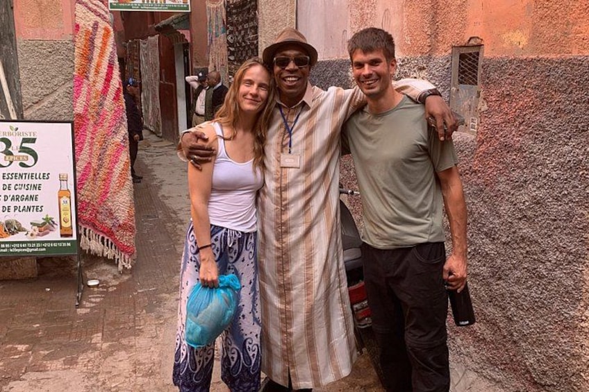 Three people standing in a narrow alleyway with a signboard and patterned fabrics in the background. 2