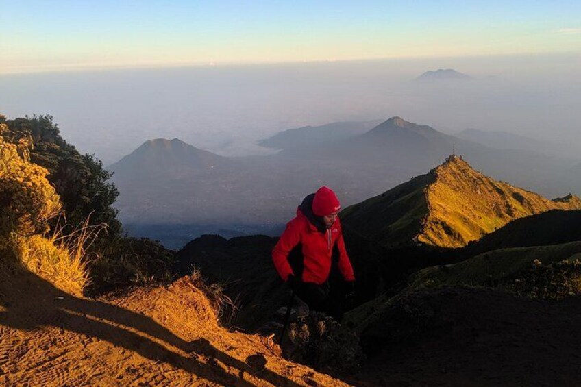 A person hiking on a mountain trail with a view of distant mountains and a clear sky. 2